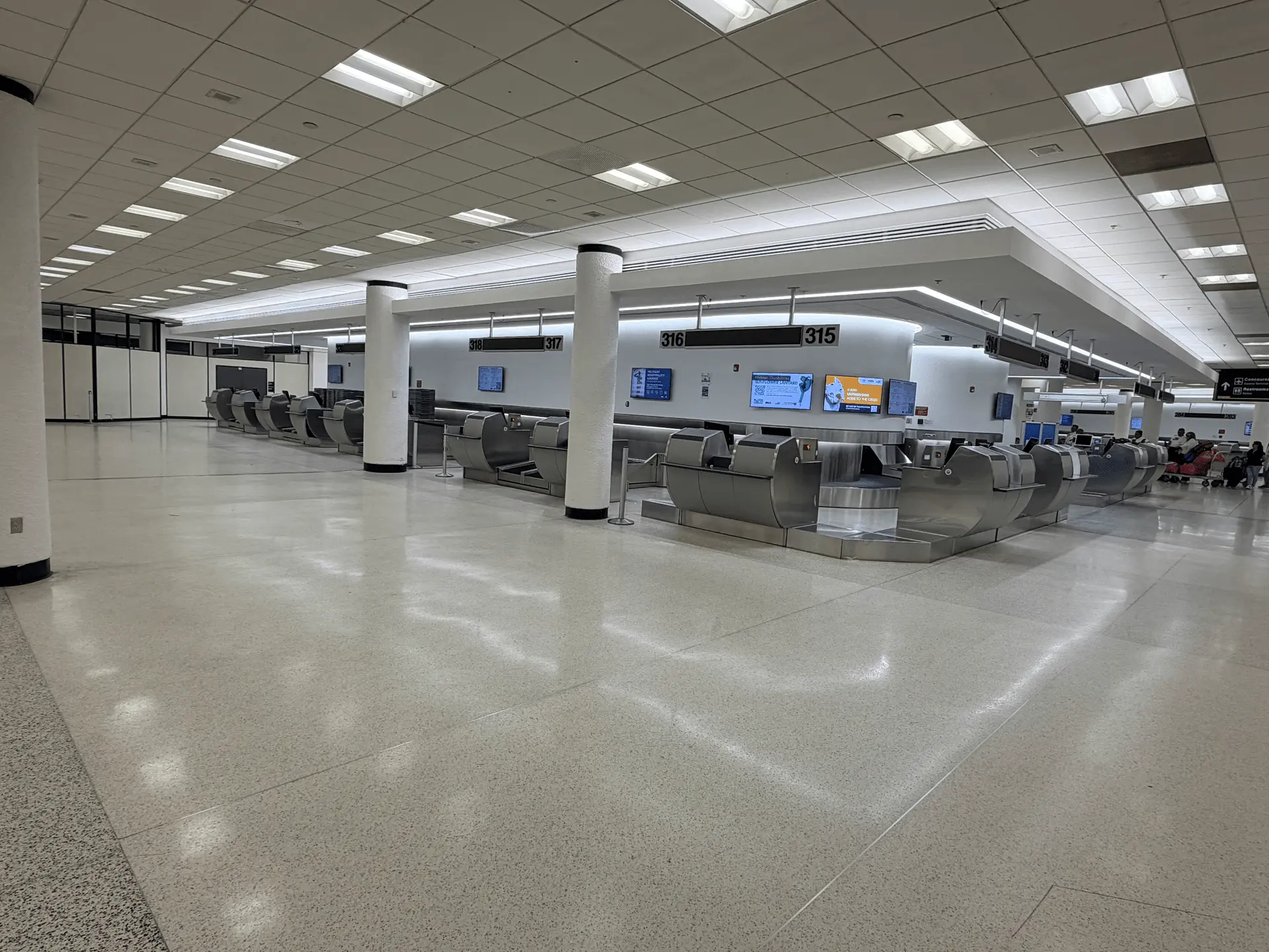 Completed check-in counters at the Miami International Airport ticket counter buildout, with stainless steel ticketing podiums, numbered counter signage, and polished terrazzo flooring.